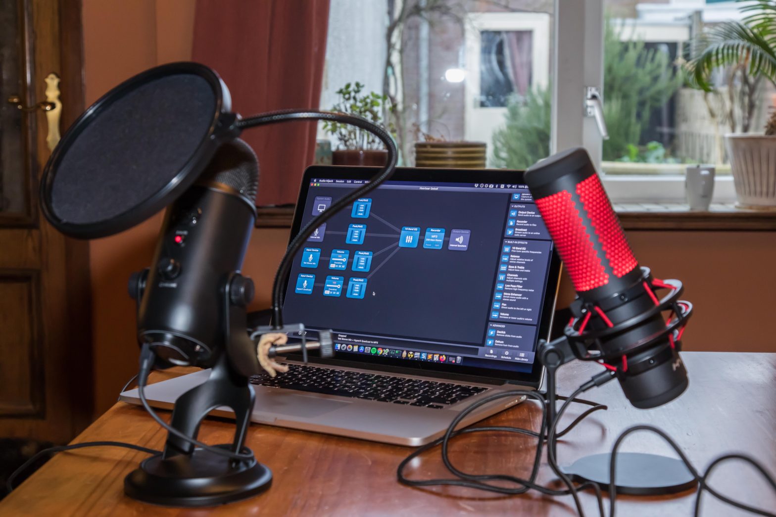 Twee studiomicrofoons op een tafel, met daarachter een macbook met op het scherm opnamesoftware.